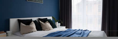 Panorama of comfortable bedroom with cozy double bed, big window and modern navy blue wallの写真素材