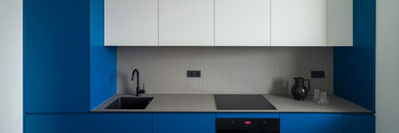 Panorama of simple, modern and small kitchen with blue and white cupboards and gray countertop and...