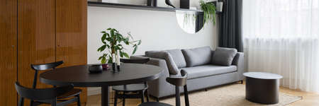 Panorama of eclectic style living room with modern black dining table with chairs, stylish couch, coffee table and decorations and big, vintage wardrobeの写真素材