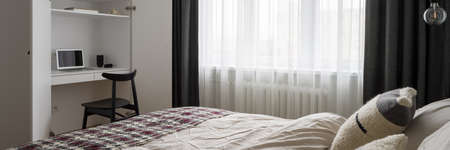 Panorama of stylish bedroom with comfortable bed and big window and desk to work in white wardrobeの写真素材