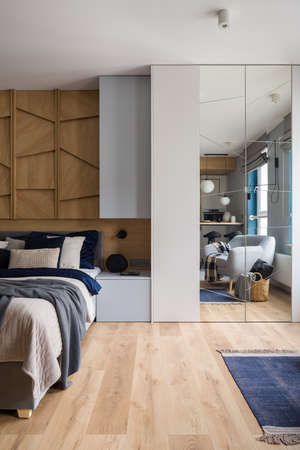 Spacious bedroom with big wardrobe with mirror, cozy bed and wood decorの写真素材