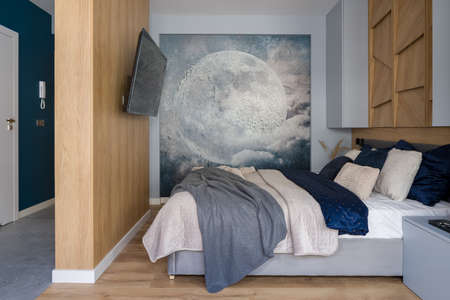 Bedroom with wooden wall and moon wallpaper, big tv and comfortable bed with stylish bedclothesの写真素材