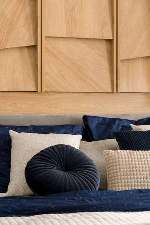 Close-up on stylish pillows on bed in bright bedroom with wooden decoration on wallの写真素材