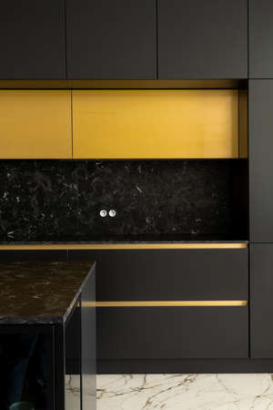 Luxury kitchen with black furniture and golden drawer handle and upper cupboards, white marble floor and black marble countertops and backsplashの写真素材