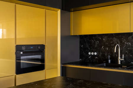 Fancy kitchen with black and gold cupboards, black marble countertops and backsplash, oven and modern silver tap in black sinkの写真素材