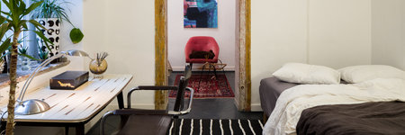 Panorama of eclectic bedroom with single bed, simple desk with chair next to window and doors to next room with red chairの写真素材