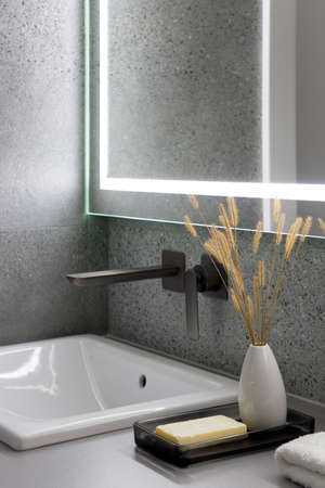 Close-up on stylish bathroom washbasin with black tap and mirror with led light and nice vase with dried grass and natural soap barの写真素材