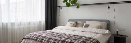 Panorama of simple decorated bedroom with big comfortable bed, modern bedside table and big window behind white curtainsの写真素材
