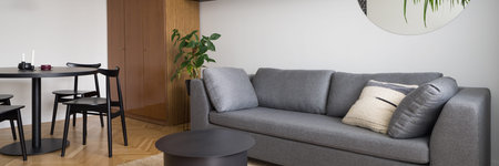 Panorama of eclectic room with cozy gray couch, modern coffee table, stylish dining table with...
