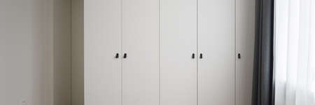 Panorama of modern, white wardrobe wall next to window with white and gray curtainsの写真素材