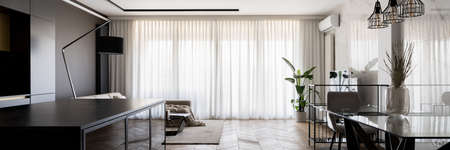 Panorama of bright apartment with kitchen and dining room open to living room with big windows behind white curtainsの写真素材