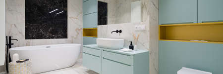 Panorama of spacious and elegant bathroom with oval bathtub, washbasin, new designed blue and gold furniture and marble floor and wall tilesの写真素材