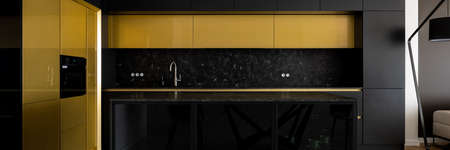 Panorama of luxury and modern kitchen with black and gold cupboards and marble countertops and backsplashの写真素材