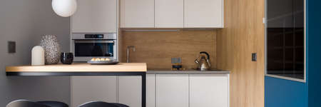 Panorama of stylish and modern kitchen with white furniture, wooden table with two chairs and wood decor on walls and backsplashの写真素材