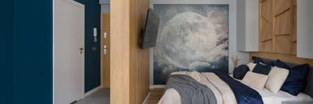 Panorama of stylish bedroom with comfortable bed, wooden walls and decorative wall mural next to corridor with blue wall and white doorの写真素材