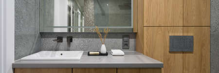 Panorama of modern design in bathroom with white square washbasin, big mirror, wooden cabinets and terrazzo tilesの写真素材