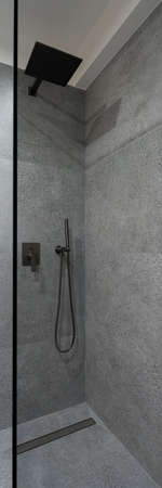 Vertical panorama of modern shower area with glass wall and granite tiles on wall and floor and with black tapの写真素材
