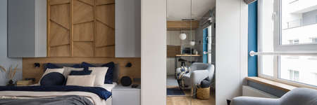 Panorama of stylish studio apartment with open bedroom, big window, comfortable bed, wardrobe with mirror and cozy armchairの写真素材
