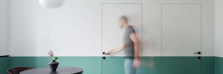 Panorama of man opening doors in dining room with white and mint green walls and doors and black table with nice vaseの写真素材