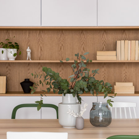 Close-up on decorative vases with plants on wooden table and wooden shelf with books and decorations in backgroundの写真素材