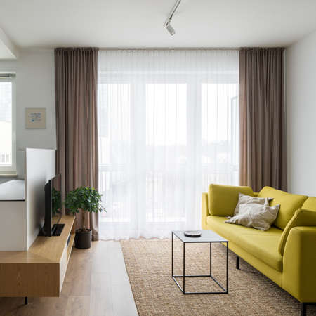 Modern designed and colorful living room with big window behind decorative curtains, yellow sofa and tvの写真素材