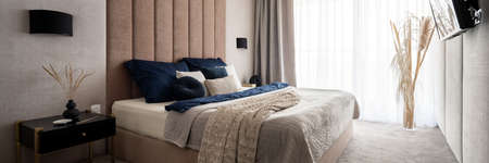 Panorama of elegant and comfortable bedroom with big window, big cozy bed with nice and decorative bedclothes and upholstered wallの写真素材