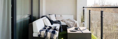 Panorama of comfortable balcony with big window doors to apartment and stylish rattan corner sofa with decorative pillows and rattan coffee tableの写真素材