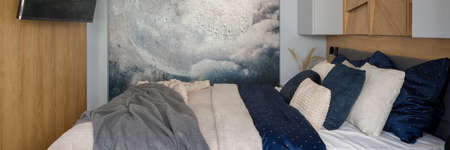 Panorama of small bedroom with wooden walls, comfortable bed with nice bedclothes and poster with moonの写真素材