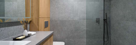 Panorama of modern bathroom with shower behind glass wall, gray terrazzo style tiles and wooden furnitureの写真素材