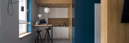 Panorama of small and modern kitchen with white cupboards, wooden wall and table with two chairsの写真素材