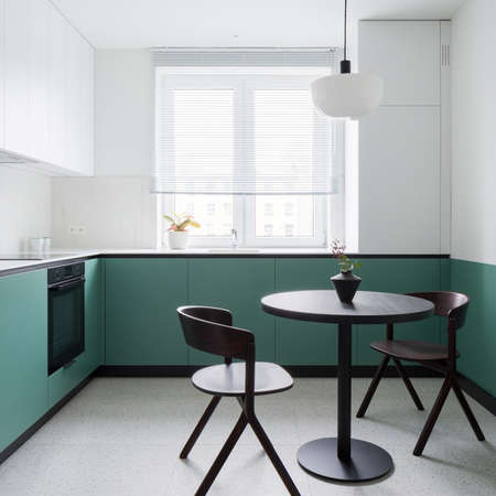 Small and modern kitchen with stylish terrazzo floor, trendy, black dining table with two chairs and stylish white and green walls and cupboardsの写真素材