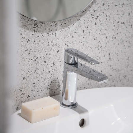 Close-up on simple silver tap in modern bathroom washbasin and with natural soap bar and stylish terrazzo wall tilesの写真素材