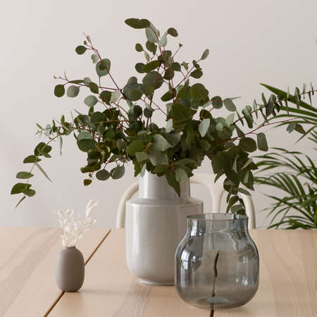 Close-up on stylish wooden table with delicate and elegant decorations, glass pot and ceramic vase with eucalyptus twigsの写真素材