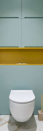 Vertical panorama of white toilet in lavatory with marble tiles on floor and blue cabinets with gold shelfの写真素材