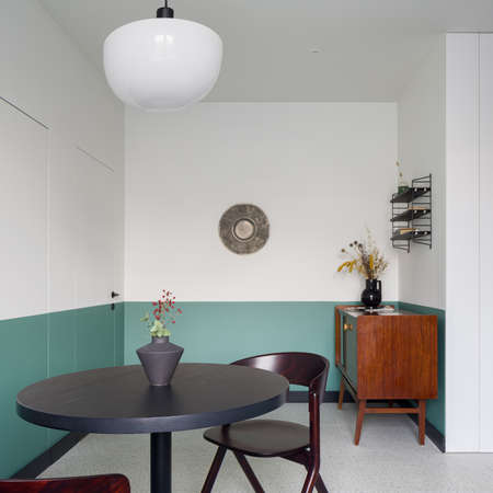 Stylish dining room with dark, round table with two chairs, with white and green walls and wooden, vintage cupboardの写真素材