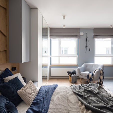 Stylish and bright bedroom with cozy bed with nice bedclothes and pillows, big windows and comfortable armchairの写真素材