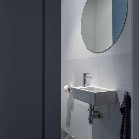 Small and simple white washbasin under big, round mirror in bathroom with gray tilesの写真素材