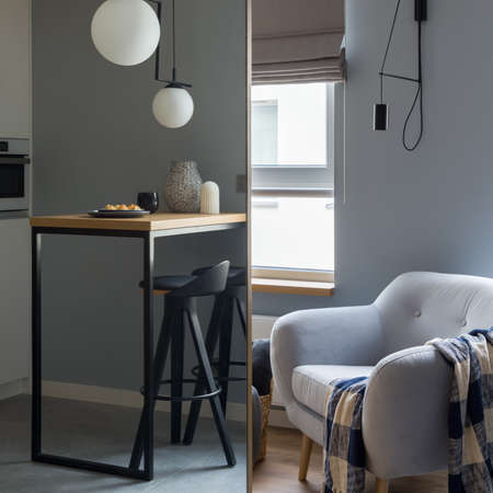 Small, wooden kitchen table with two chairs and cozy, gray armchair in mirror reflectionの写真素材