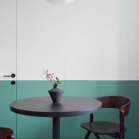 Modern dining room with stylish, black and round dining table with decorative vase and dark wooden chairの写真素材
