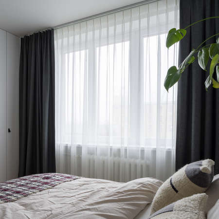 Bright bedroom with king size bed and stylish bedclothes and with big window behind decorative white and black curtainsの写真素材