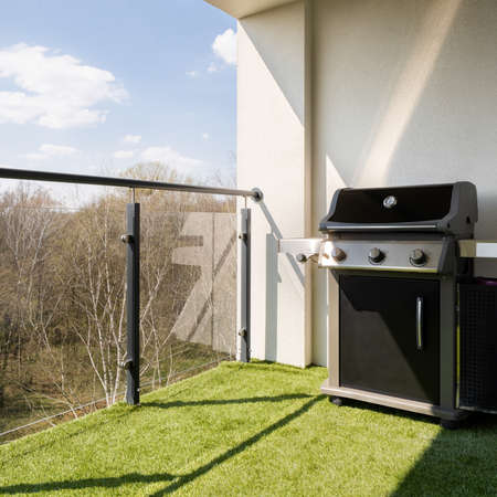 Spacious terrace with modern glass balustrade, synthetic grass and stylish gas grillの写真素材