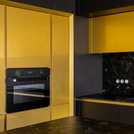Close-up on oven in fancy kitchen with black and gold cupboards, black marble countertops and backsplashの写真素材