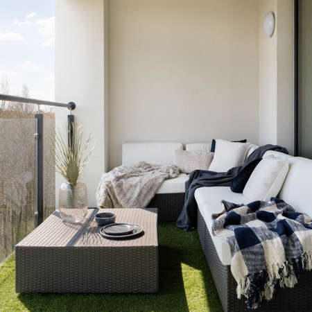 Stylish balcony with fake grass and comfortable, rattan corner sofa with pillows and blankets and square coffee tableの写真素材