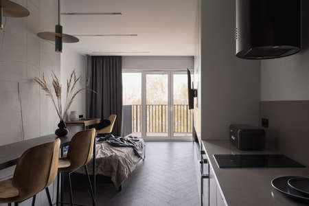 Small and stylish kitchen in open studio apartment with wooden floor and window wallの写真素材