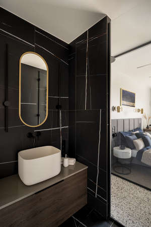 Elegant bathroom with black tiles and glass wall next to bedroomの写真素材