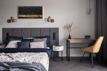 Comfortable and stylish bedroom with cozy bed, stylish bedclothes and functional desk with yellow chairの写真素材