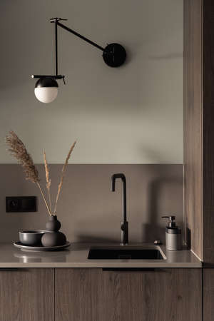 Close-up on stylish kitchen countertop with simple wooden furniture, black sink and tap and decorationsの写真素材