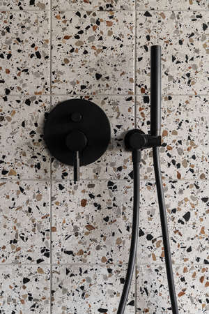 Close-up on modern, black shower tap mounted in wall with small terrazzo style tilesの写真素材
