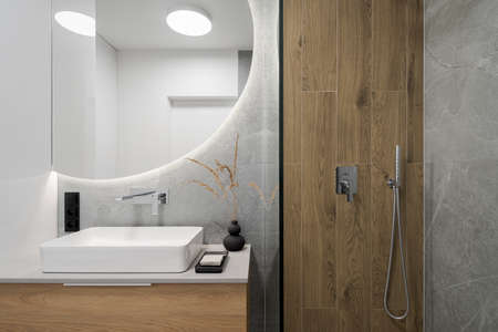 Modern bathroom with wooden style tiles in shower cabin next to big, round mirror with led light above washbasinの写真素材
