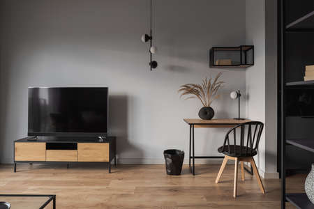 Small wooden desk with stylish decoration and chair next to tv on wooden sideboard in spacious living roomの写真素材